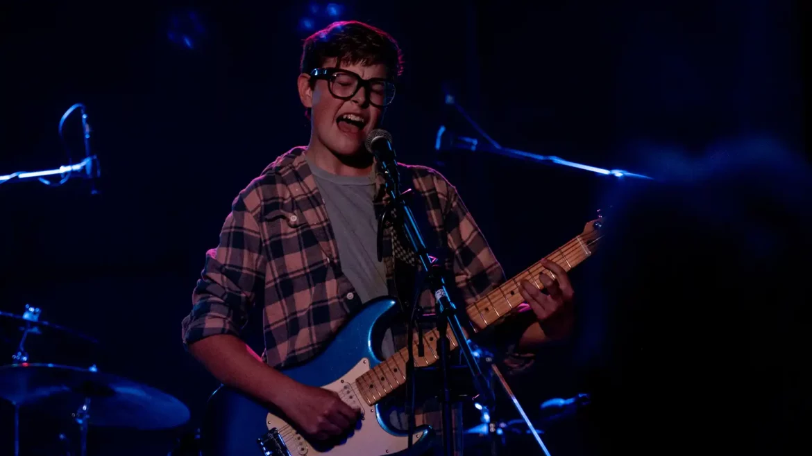 Carson Ferris passionately performing on stage, strumming his guitar and singing into a microphone.