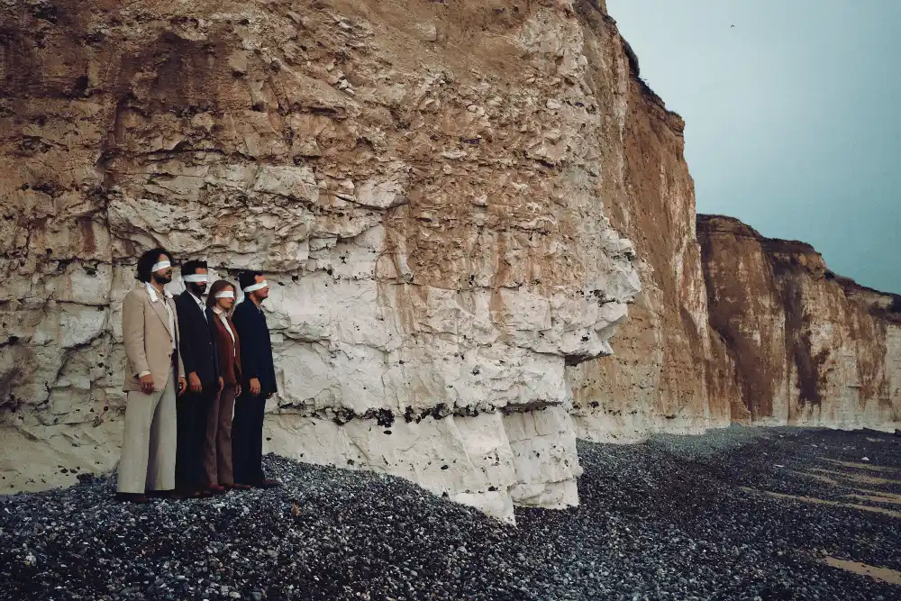 At Mos band stands blindfolded against towering cliffs.