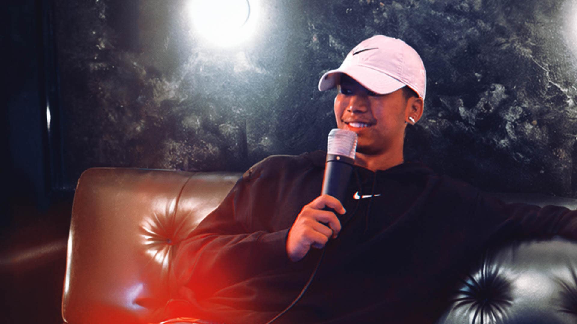 Smiling R&B singer Phurpax holding a microphone, relaxing on a couch.