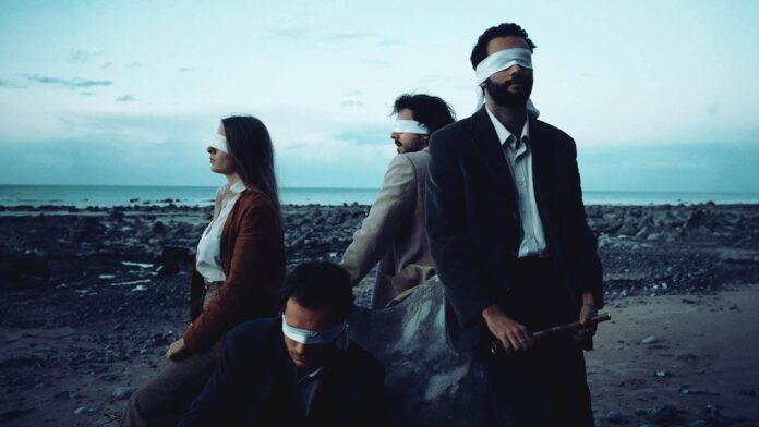 Band members of At Mos blindfolded on a beach at dusk.