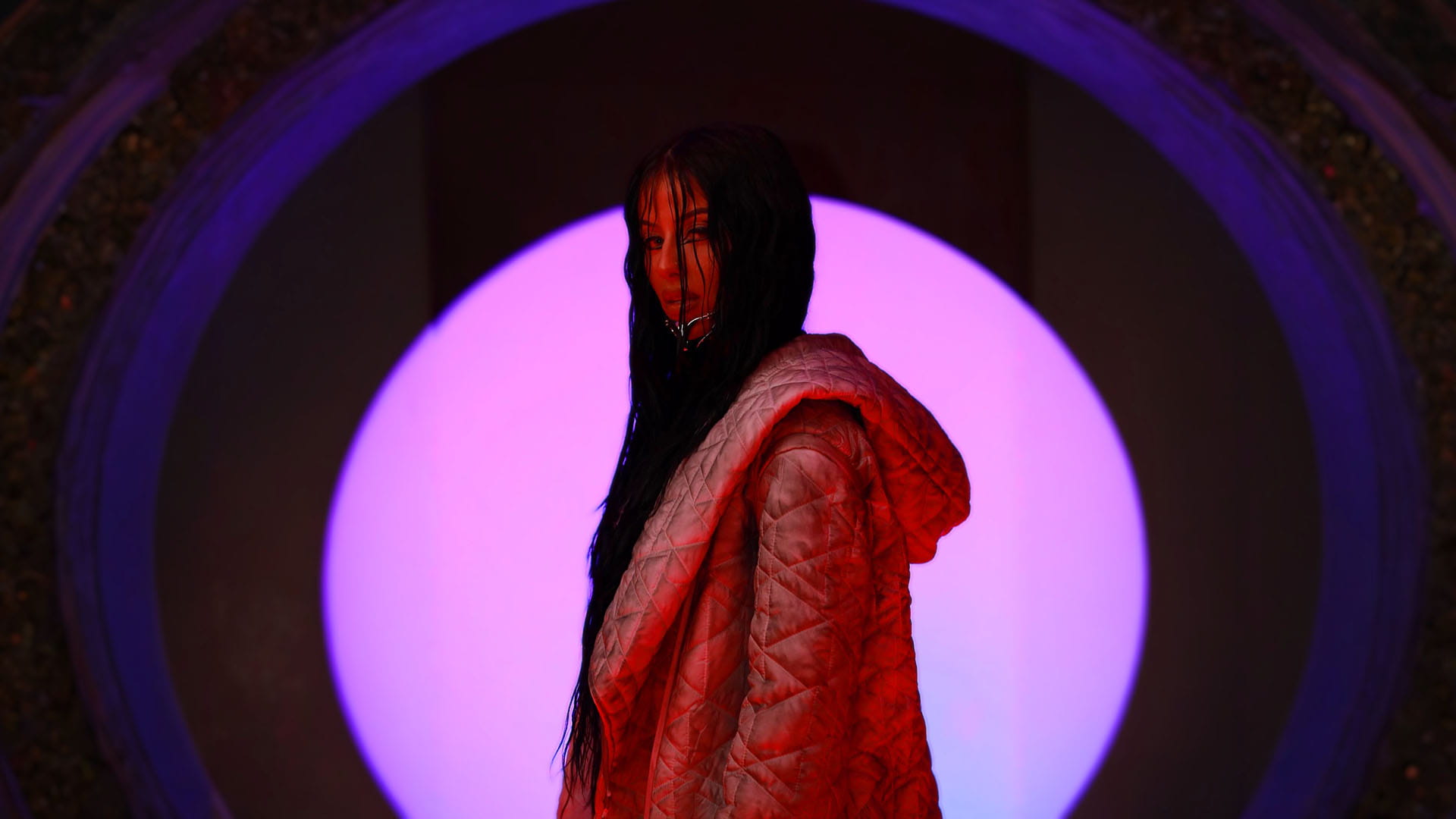 SAGEALINA in profile, wearing a textured jacket, against a glowing pink orb backdrop.
