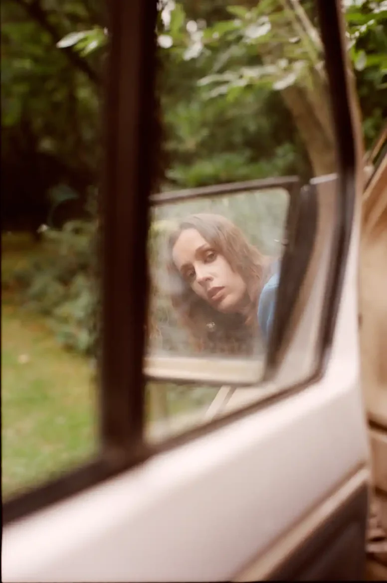 Reflective image of pop artist Sophie Kilburn seen through a van's side mirror, gazing thoughtfully