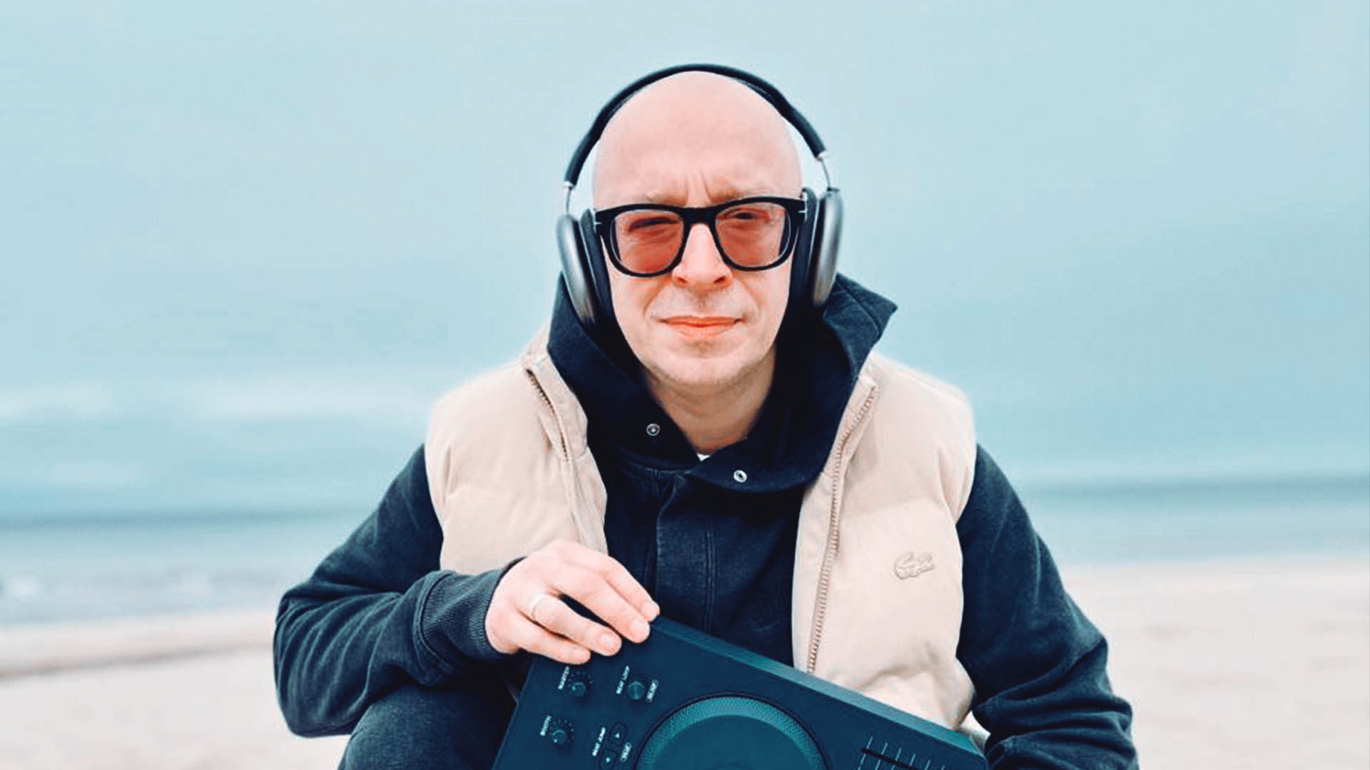 DJ Remo holding a MIDI controller on a beach, symbolizing his return to music production.