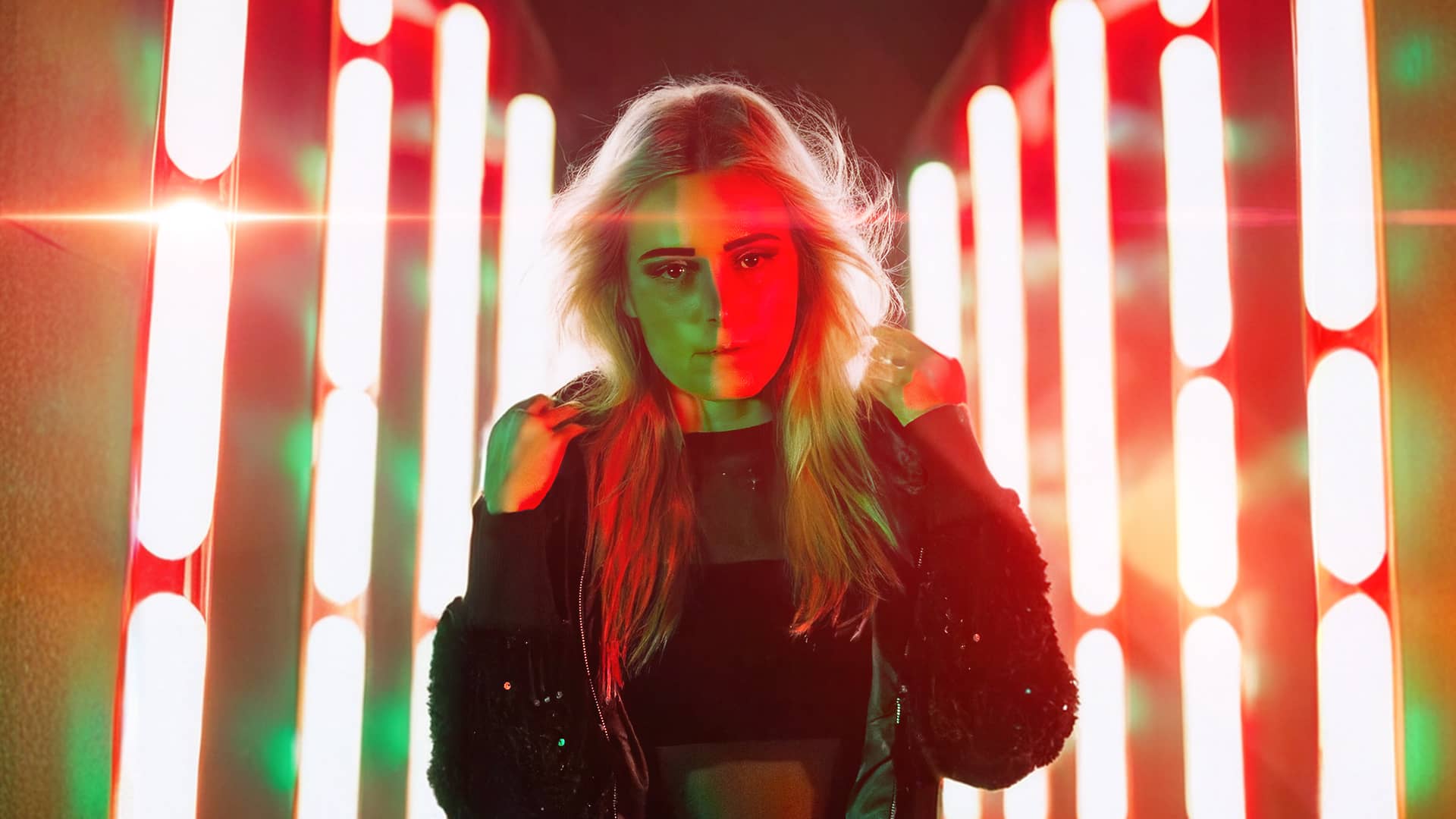 DJ Oskana stands amid vibrant neon lights, embodying the lively spirit of her song 'Extasy'.